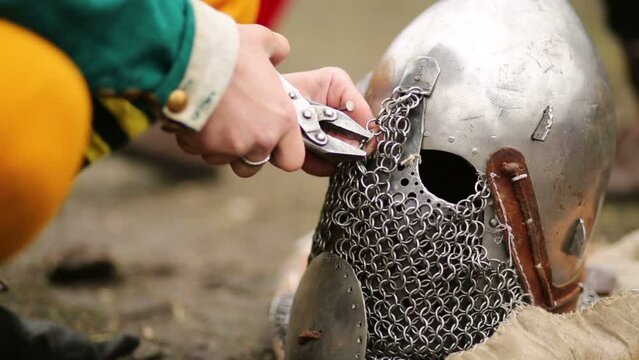 Hands of man in medieval costume repairing chain of metal helmet