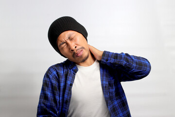 Asian man, dressed in a beanie hat and casual outfit, is suffering from neck and shoulder pain, isolated on a white background. Illustrating healthcare and problem concepts