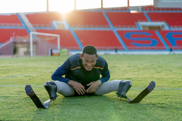 Sport man athlete prosthesis legs sit down on grass field and separate his legs also bend down the...