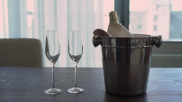 Bottle of expensive champagne in metal ice bucket. Cold sparkling white wine in apartment, hotel or restaurant. A luxurious life, alcoholic drink, a holiday. Glasses.