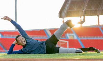 Sport man athlete prosthesis legs lie on his side down on grass field and raise one of his legs up...