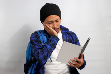 A pensive young Asian student, dressed in a beanie hat and casual shirt, carrying a backpack and holding a notebook, is engrossed in tackling a challenging assignment, deep in thought, exploring ideas