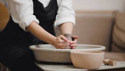 Hands of young girl with manicure master on potter wheel makes clay dishes. Art workshop place for...