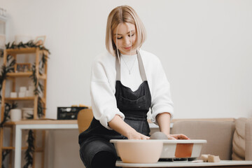 Happy young woman on potter wheel makes clay dishes, relax DIY business.