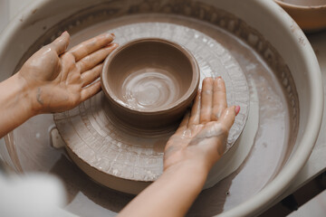 Hands of young girl with manicure master on potter wheel makes clay dishes, top view. Art workshop...