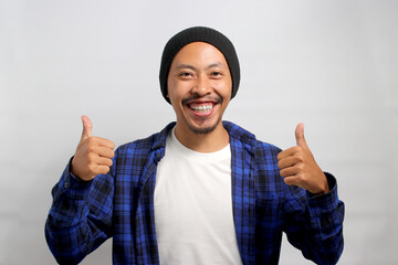 A smiling young Asian man, dressed in casual clothes and wearing a beanie hat, is giving a thumbs...