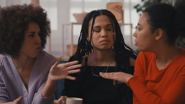 Three young women friends drinking coffee and discussing latest events on couch