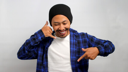 Enthusiastic young Asian man, dressed in a beanie hat and casual shirt, is gesturing a CALL ME...