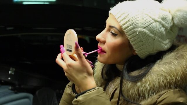Girl in warm clothes does make-up with small mirror