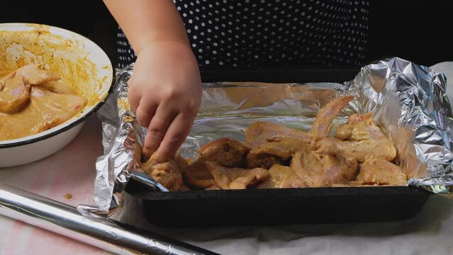 Women's hands place marinated chicken wings in spices on Olga for baking. Medium plan.