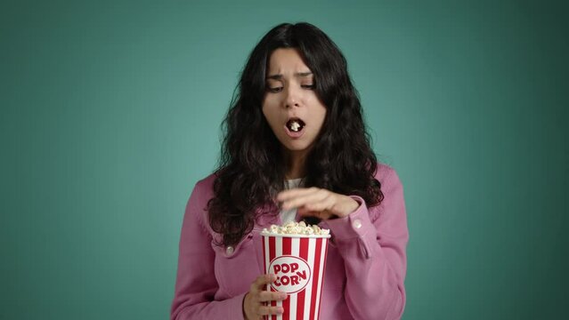 The girl with a puzzled look watches a movie. She has popcorn in her hands, which she eats non-stop. High quality 4k footage