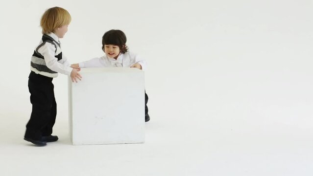 Two little boys play with large white cube in white studio