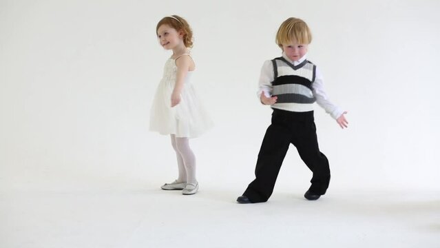 Little smiling girl in white dress and boy dance in white studio