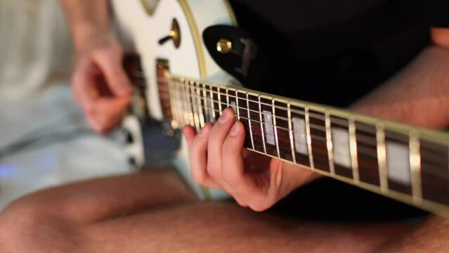 Hands of young musician yank strings of electric guitar