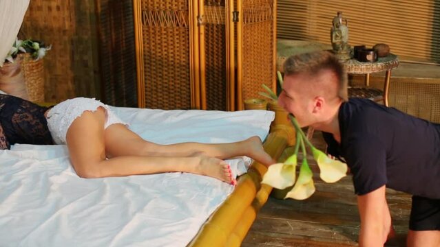 woman lies in bed and boyfriend crawls on knees with flowers