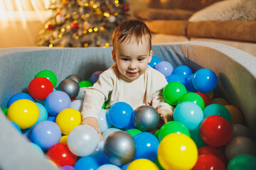Fototapeta na wymiar A cute little boy is playing in a pool of plastic balls. Children's dry pool at home.
