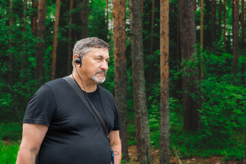 Portrait of a man in his 70s with a radio guide earpiece in the woods. Travelling pensioners....