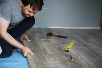 Installing laminated floor, detail on man hands blue wooden tile, over white foam base layer, small...