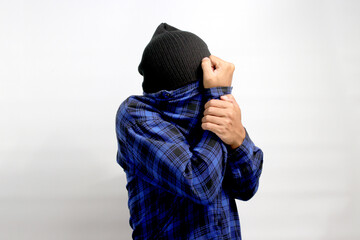The amusingly frightened young Asian man hides his face with his shirt, expressing a mix of fear,...