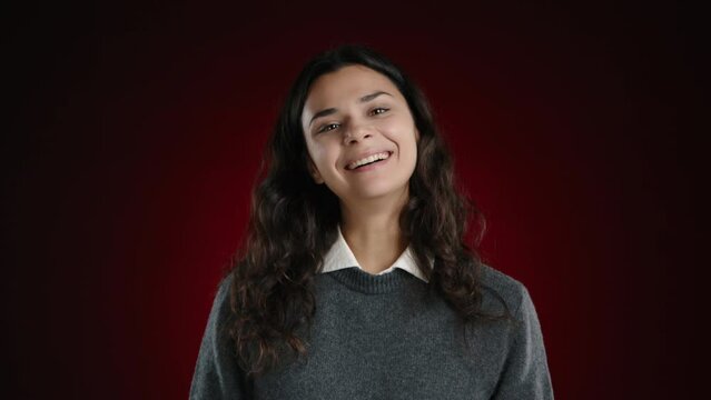 The girl is laughing hysterically, looking into the camera, unable to stop her laughter. She is on a dark red background. High quality 4k footage
