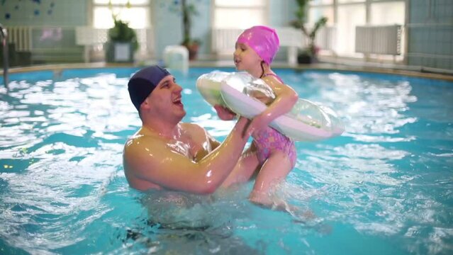 Father raises his daughter with inflatable tube in swimming pool 