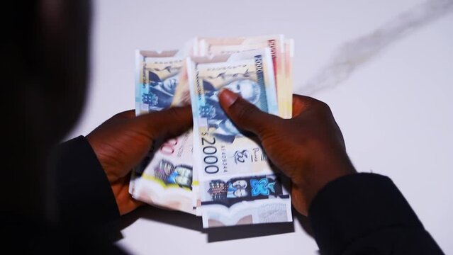 over the head shot of Black male in black long sleeves shirt counting Jamaican dollar notes