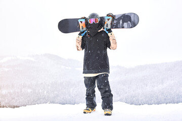 Snowboarder on the hill. Shot of the man snowboarder holding board on his shoulders and looking...