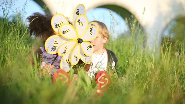 girl and boy sit on green grass and play with wind spinner