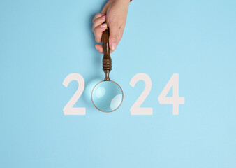 A female hand holds a magnifying glass and the inscription 2024