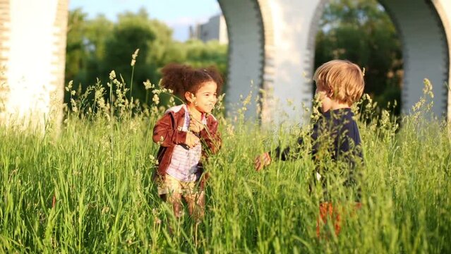 Little boy and girl have fun among grass at summer day