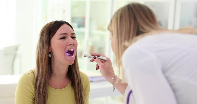 Ent doctor examines throat of female patient and shines flashlight