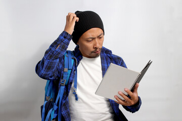 A confused young Asian student, dressed in a beanie hat and casual shirt with a backpack, scratches...
