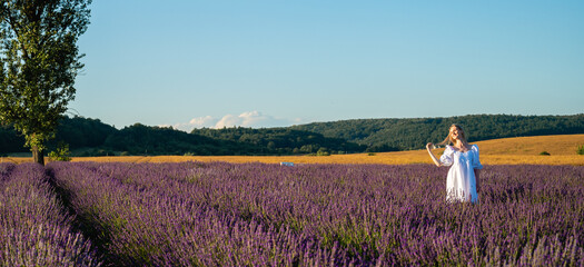 panoramic photo of relaxed young girl in white dress, in thought, breathing fresh air, sitting in lavender field on sunny day, looking away, thinking, rear view