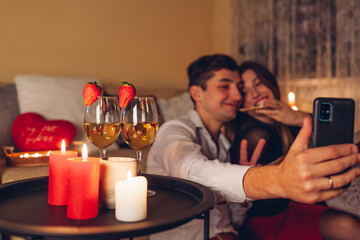 Valentines Day loving couple taking selfie on phone by wine glasses with candles having pizza...