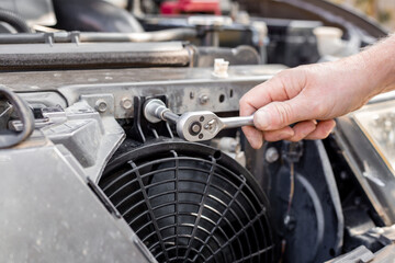 A man fixes an engine cooling fan under the radiator grill of a car. Machine maintenance and repair