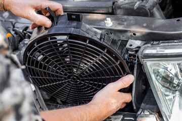 A man inserts an engine cooling fan under the radiator grill of a car. Machine maintenance and repair