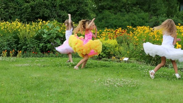 Four little girls in lush skirts turn near flowerbeds in park
