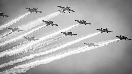 A formation of stunt planes trailing smoke in a fly past in black and white at an airshow on the...
