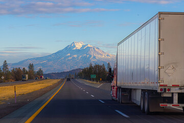 A semi tractor trailer truck drives on the Interstate in California with Mount Shasta in the...