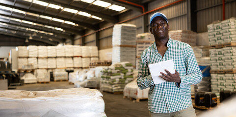 Portrait of african-american man, construction material storage worker, standing inside warehouse. Man with documents in storage room.