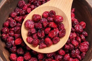 Red dried cranberries fruits in wooden spoon in rustic bowl.
