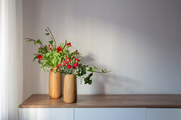 red carnations and tulips in modern vases on background gray wall