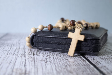 Rosary with cross laying on old Holy Bible book on rustic wooden table. - obrazy, fototapety, plakaty