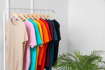 Rack with colorful t-shirts near light wall