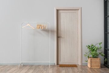 Rack with wooden hangers and houseplant near light wall in room