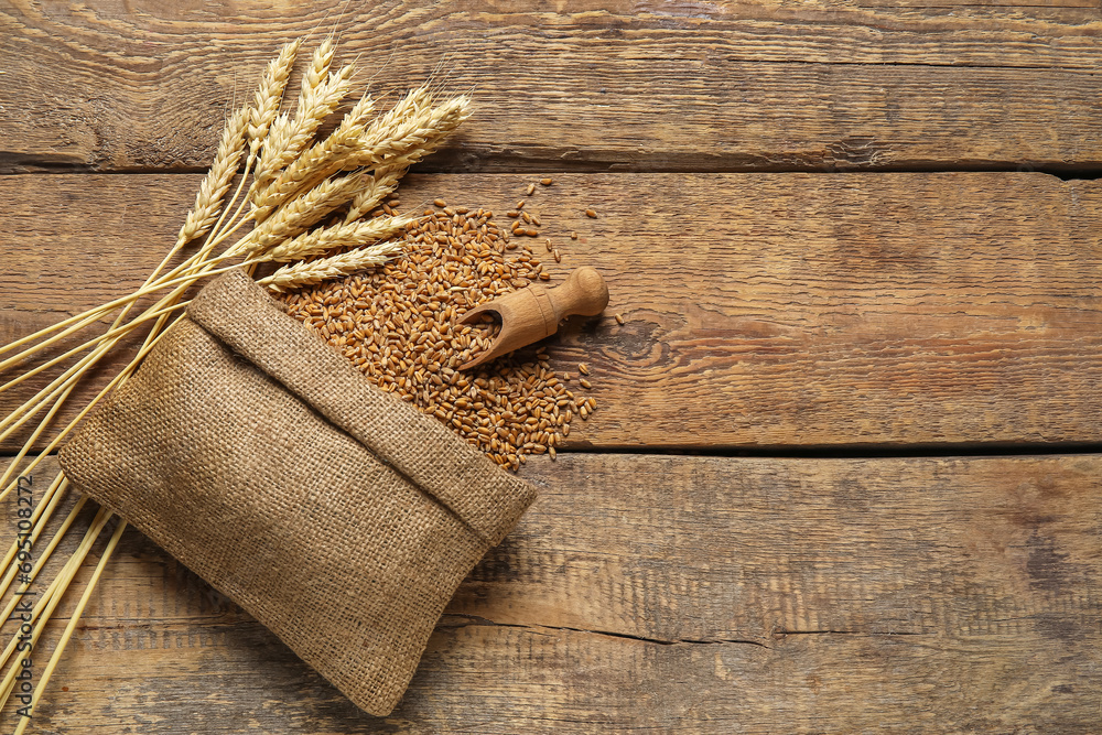 Wall mural Sack with wheat grains, ears and scoop on wooden background