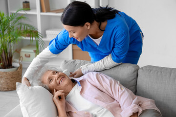 Female nurse caring about lying senior woman at home - obrazy, fototapety, plakaty