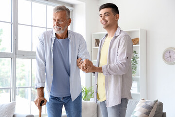 Young man helping his father to walk at home