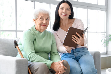 Senior woman and her daughter with book at home - obrazy, fototapety, plakaty