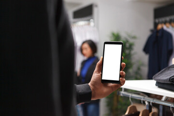 Clothing store buyer holding smartphone blank touchscreen in hand while shopping for apparel....